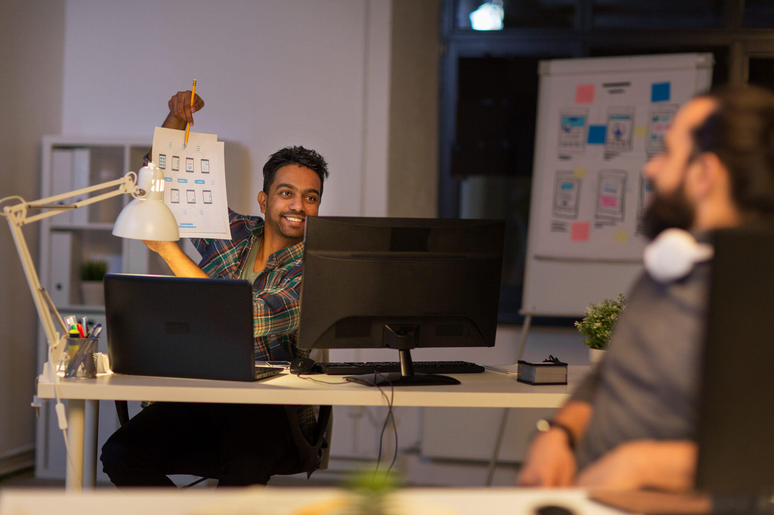 business deadline and web design people concept happy creative man showing papers to colleague at night office